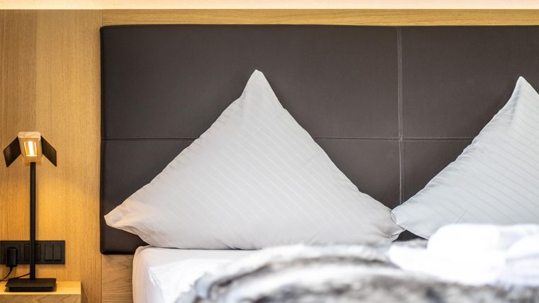 A modern bedroom with a large bed and stylish pillows. Next to the bed is an elegant bedside lamp.