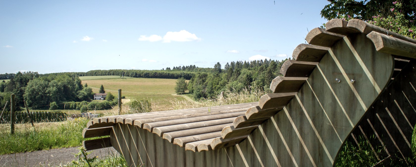 Holzliegebank mit Blick auf gr&uuml;ne Felder und W&auml;lder unter blauem Himmel in Neidenbach., &copy; TI Bitburger Land - Monika Mayer