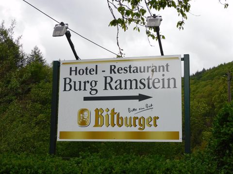A sign for the Hotel and Restaurant Burg Ramstein. It shows the direction to the castle and includes the Bitburger logo.