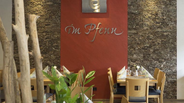 Ein stilvolles Restaurant mit Holztischen und einer warmen Atmosphäre. Die Wand ist mit rotbrauner Farbe und dekorativen Steinen gestaltet.