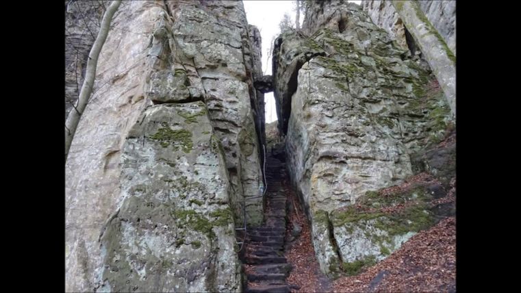 A narrow passage between tall, moss-covered rocks. A staircase leads up through the crevice.