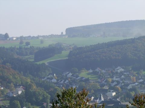 A picturesque landscape with gentle hills and a small village in the foreground. The surroundings are green and wooded, ideal for nature lovers.