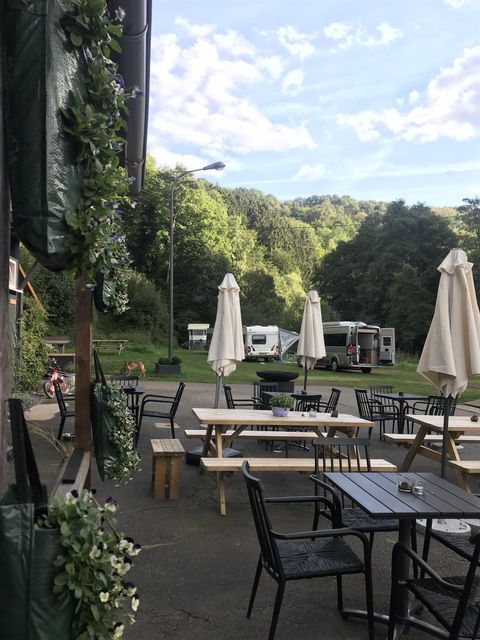 Un espace extérieur accueillant avec des tables et des chaises. En arrière-plan, on peut voir des collines vertes et des camping-cars.