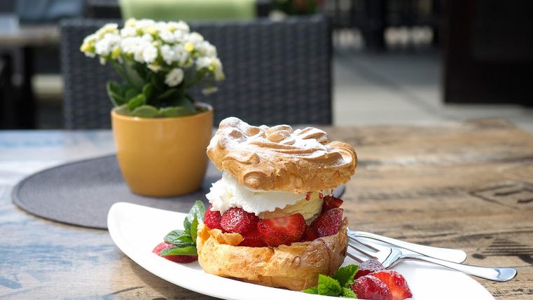Ein köstliches Dessert mit einer Schicht aus Baiser, Sahne und frischen Erdbeeren. Im Hintergrund steht ein blühender Topfpflanze.
