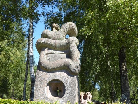 An impressive stone sculpture surrounded by trees. The sculpture displays significant shapes and textures in the sunlight.