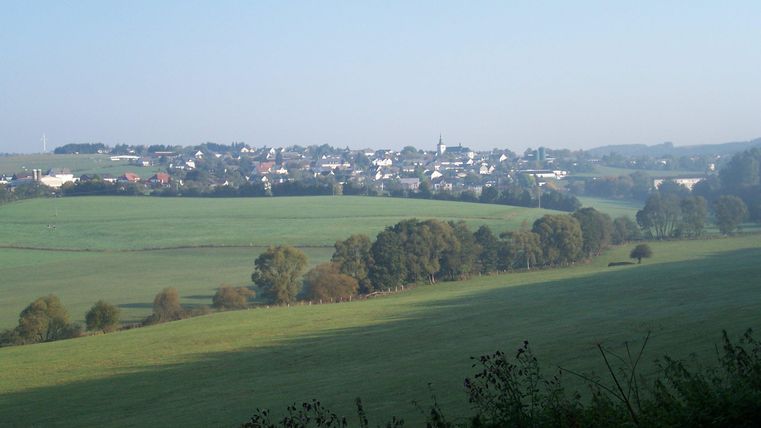 A peaceful landscape with gentle hills and a small village in the background. The sky is clear and the day seems to be calm.