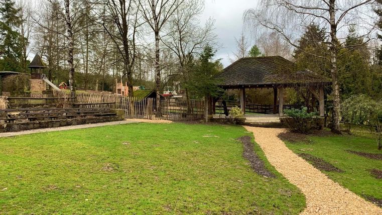 Eine grüne Wiese mit einem Kiesweg und einem Pavillon im Hintergrund. Umgeben von Bäumen und einem ruhigen Park.