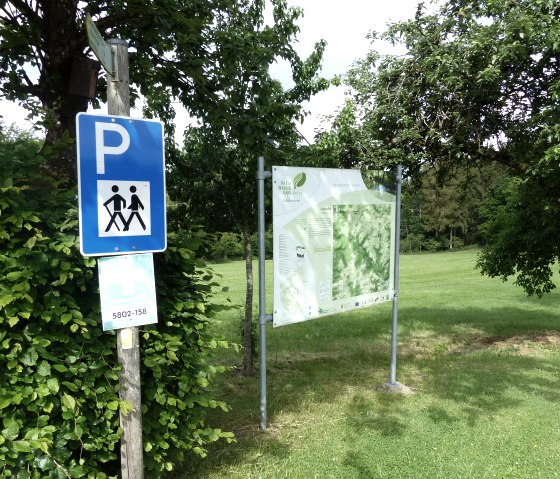 Parkeerbord voor wandelaars naast een informatiebord in een groene, bosrijke omgeving. Zonnige dag, bomen en weiland op de achtergrond., &copy; Tourist-Information Islek, Ingrid Wirtzfeld