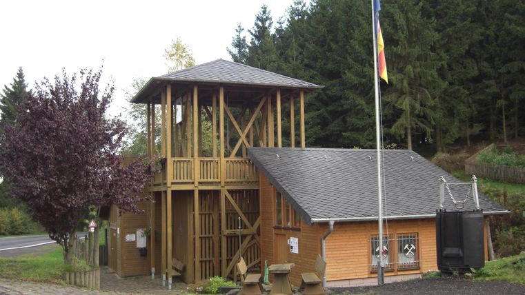 A wooden building with a viewing platform and a flagpole. It is located in a natural environment with trees in the background.