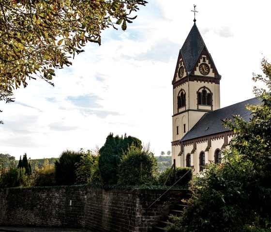 L'&eacute;glise St. Remigius &agrave; Oberweis, entour&eacute;e d'arbres et d'un mur de pierre, sous un ciel nuageux., &copy; TI Bitburger Land