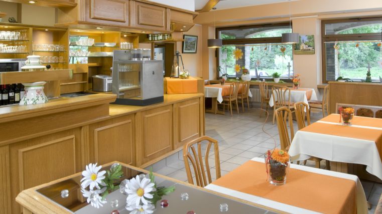 Ein gemütliches Restaurant mit Holzdekor und hellen Farben. Die Tische sind schlicht gedeckt und bieten eine einladende Atmosphäre.