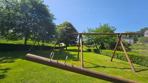Un beau terrain de jeu avec des balançoires dans une prairie verte. Le ciel est clair et bleu, entouré d'arbres.