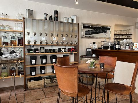 Un café confortable avec des meubles en bois et une étagère pleine de thés et d'épices. Les murs sont clairs et l'atmosphère est accueillante.