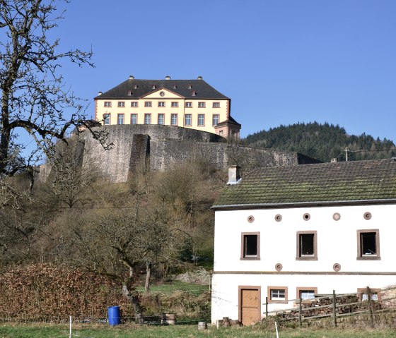 Schloss Malberg thront auf einem H&uuml;gel, umgeben von einer Steinmauer. Im Vordergrund steht ein wei&szlig;es Haus mit gr&uuml;ner Dachbedeckung., &copy; TI Bitburger Land