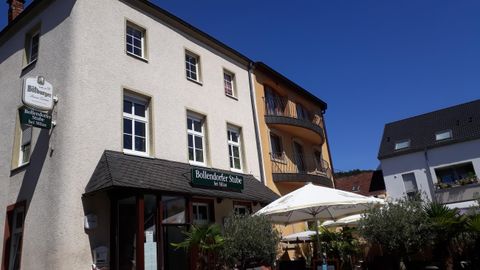 A charming building with several windows and an entrance. There are sun umbrellas and plants in front of the house.