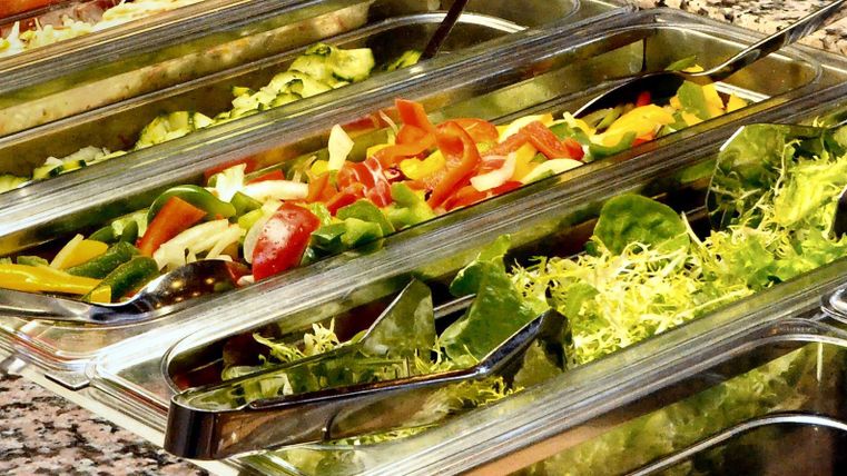 Ein Buffet mit frischem Gemüse und Salat in klaren Behältern. Die Auswahl umfasst verschiedene Sorten von Salat und geschnittenem Gemüse.