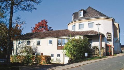 A modern building with a round roof and several windows. It is located on a quiet street, surrounded by trees and shrubs.