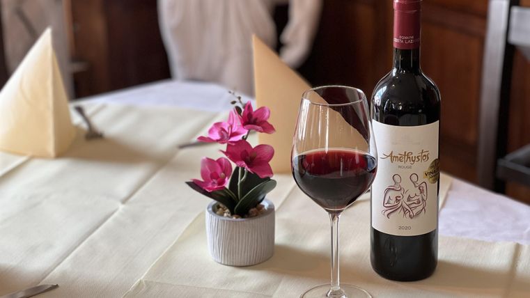 A laid table with a glass of red wine and a bottle of wine. A small plant with pink flowers complements the arrangement.