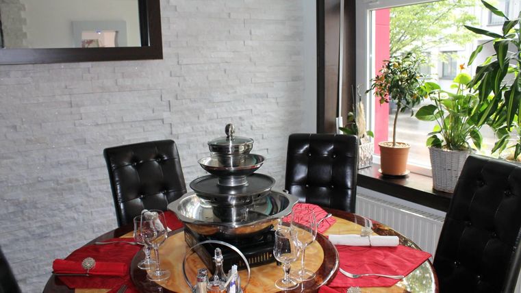A cozy dining area with a round table and black chairs. In the center is a fondue pot, surrounded by glasses and red napkins.