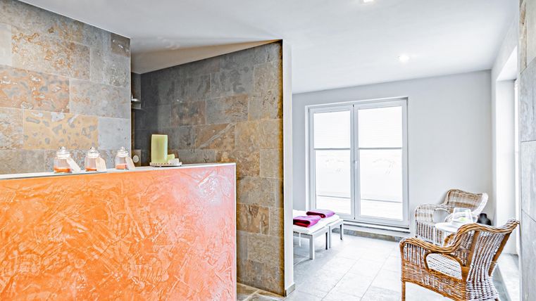 A modern wellness area with an orange reception desk. There are cozy rattan chairs and large windows that provide plenty of daylight.