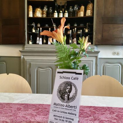 An inviting café interior with a table decoration of flowers and a menu board. In the background, shelves with various bottles and glasses can be seen.