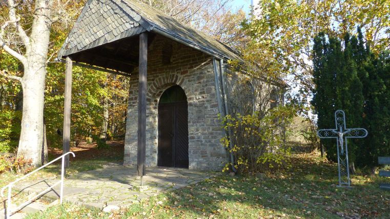 Un petit bâtiment en pierre avec un toit en ardoise se trouve dans une zone forestière. Entouré d'arbres et d'espaces verts, il dégage une atmosphère calme et contemplative.