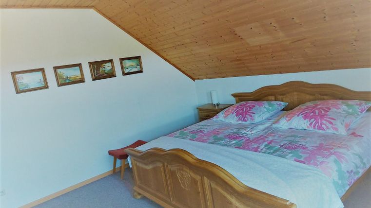 A cozy bedroom with wooden furniture and a double bed. Pictures hang on the wall, and the ceiling is sloped.