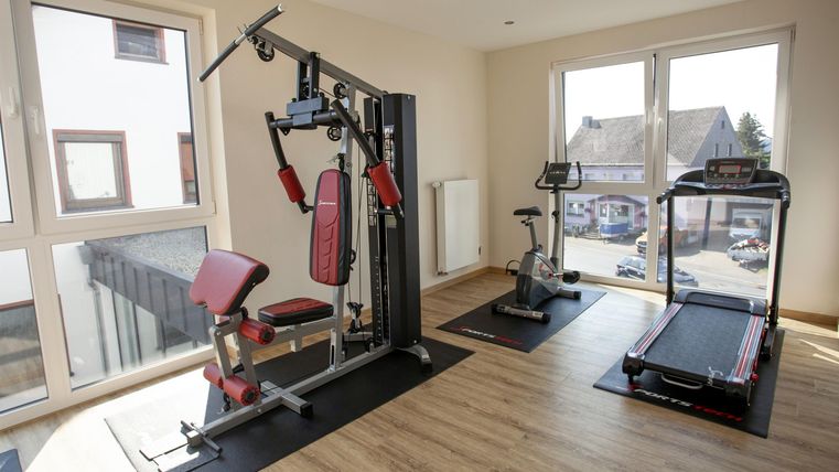 A modern gym with various training equipment. Visible are a strength machine, a treadmill, and a stationary bike.