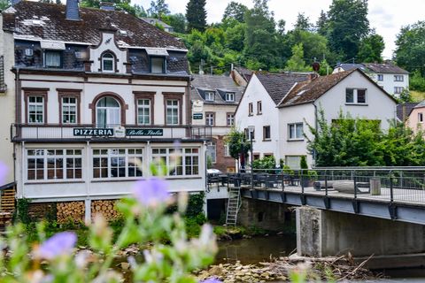 A charming pizzeria building next to a small river. In the background, more houses and trees can be seen.
