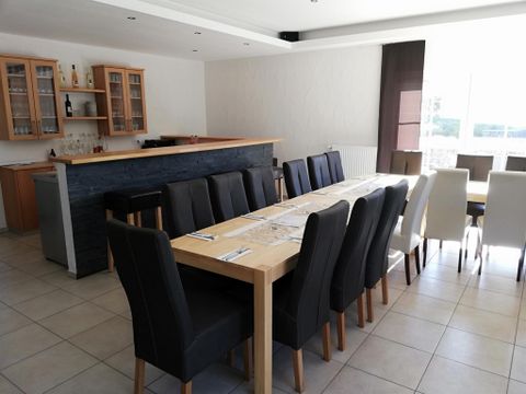 A modern dining room with a long table and comfortable chairs. The large window front ensures plenty of daylight and an inviting atmosphere.