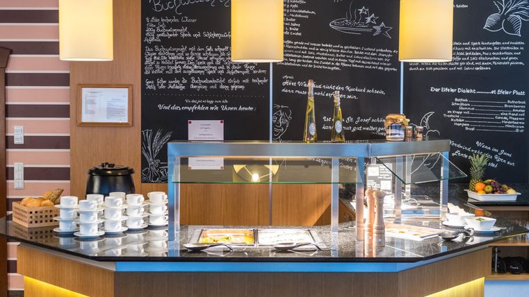 Een uitnodigende ontvangsthal met een moderne balie inrichting. Op de achtergrond zijn informatie op een bord geschreven en is servies gereedgemaakt voor het serveren.