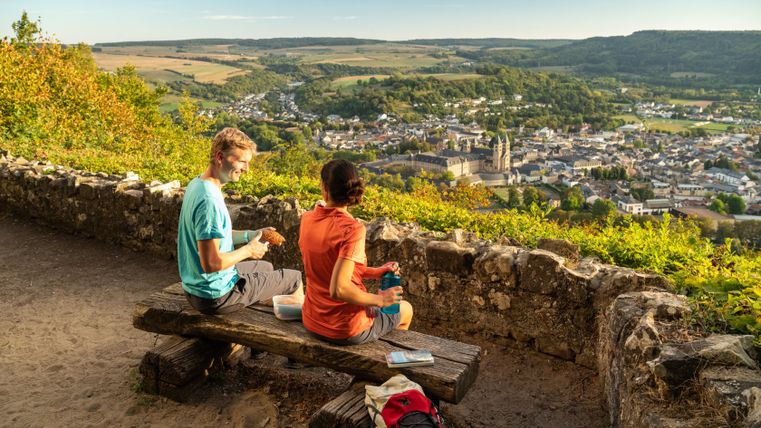 Zwei Personen sitzen auf einer Bank mit Blick auf Echternach, umgeben von grüner Landschaft.
