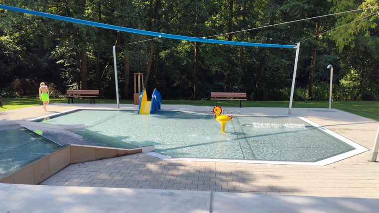 Un terrain de jeux aquatiques avec une grande surface d'eau plate. À l'arrière-plan, on peut voir des arbres et des bancs.
