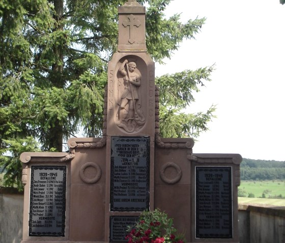 Un monument aux morts avec Saint-Georges et des inscriptions, flanqu&eacute; de fleurs, dans un d&eacute;cor d'arbres et de paysage., &copy; Conny Meier