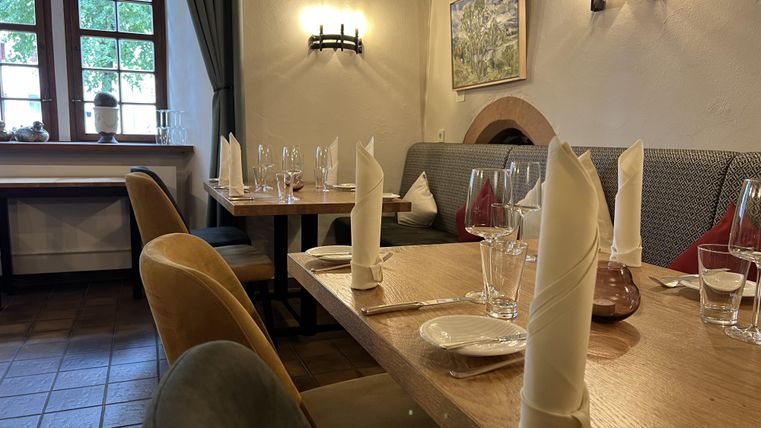 Een gezellig restaurant met mooi gedekte tafels. De muren zijn licht en er zijn ruime ramen die daglicht binnenlaten.