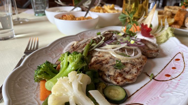 A plate with grilled fish, garnished with onions and fresh herbs. Served with a side of colorful vegetables.