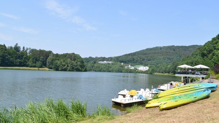 Een rustige meer met een prachtig oeverlandschap en groeiend gras. Aan de oever liggen kleurrijke kajaks en een steiger met recreatieve mogelijkheden.
