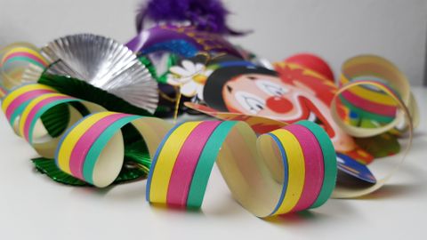 Bunte Luftschlangen und eine Clownmaske liegen auf einem Tisch. Die fröhlichen Farben bringen eine festliche Stimmung.