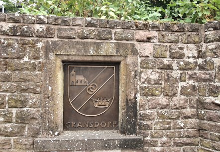 Steinwand mit einem Wappen von Gransdorf, das eine Kirche, zwei Ringe und eine Krone zeigt. Rechts ist ein Abflussrohr zu sehen., &copy; TI Bitburger Land S.Wagner