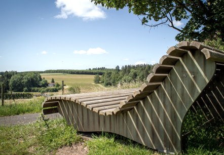 Banc de repos en bois avec vue sur des champs et des for&ecirc;ts verdoyants sous un ciel bleu &agrave; Neidenbach., &copy; TI Bitburger Land - Monika Mayer