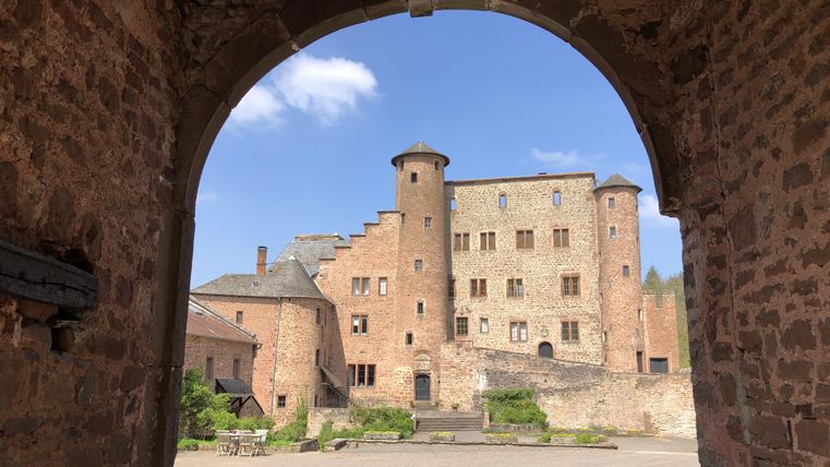 Un château historique, vu à travers une grande porte. Le ciel est bleu et le paysage est vert.