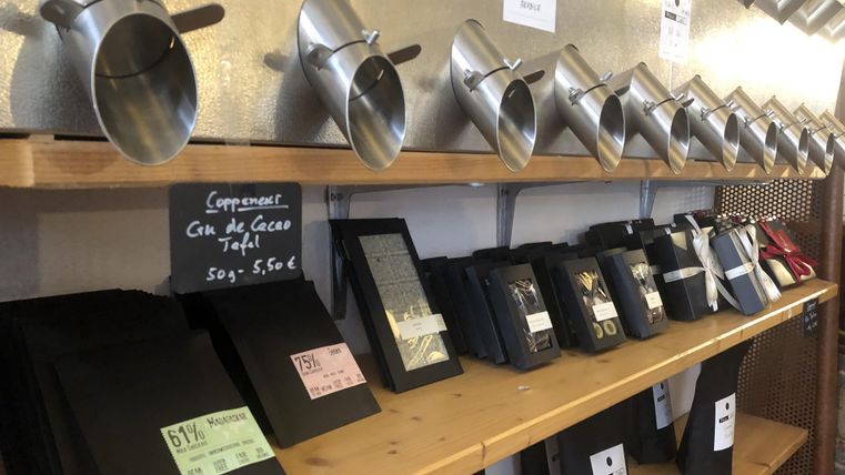 Une étagère avec des barres de chocolat et de la poudre de cacao dans différents contenants. Les produits sont disposés dans des emballages élégants et des étiquettes de prix.