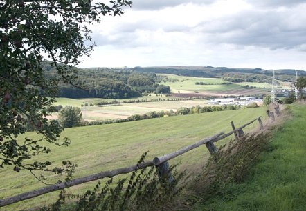 Paysage avec des prairies, des arbres et une cl&ocirc;ture en bois au premier plan. En arri&egrave;re-plan, on voit des champs et des collines sous un ciel nuageux., &copy; V. Teuschler
