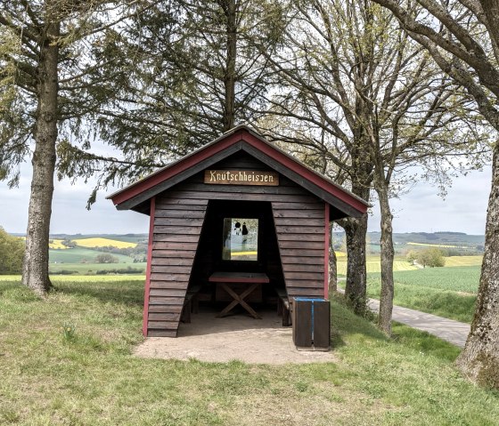 Une petite cabane en bois avec un panneau 'Knutschheisjen' se trouve entre les arbres dans un paysage verdoyant de champs et de collines., &copy; A. Girards
