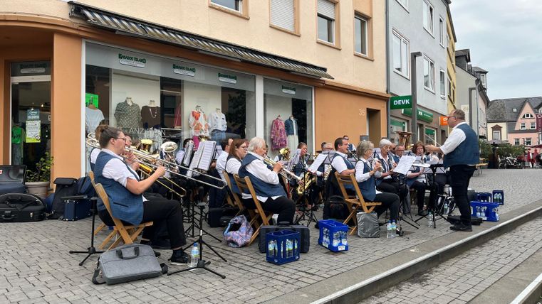 A music group is playing on the street. The musicians are sitting on chairs and are dressed in matching outfits.