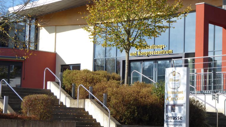 Een modern evenementen- en congrescentrum met een grote glazen pui. Voor het gebouw bevinden zich trappen en een verzorgd groenvoorziening.