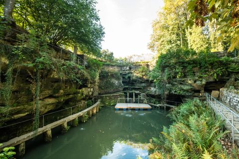 Un paysage paisible avec une eau claire, entourée de murs rocheux et de verdure luxuriante. Un pont en bois mène à une plateforme dans l'eau.
