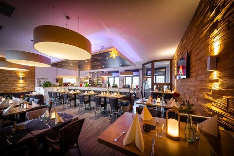 Een modern restaurant met warm licht en elegant gedekte tafels. De wanden zijn versierd met hout en de sfeer is uitnodigend en gezellig.