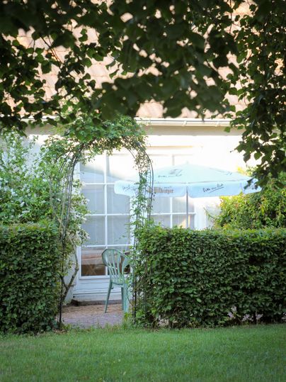 A beautiful garden with seating under a sun umbrella. A planted archway leads to the entrance door of the house.