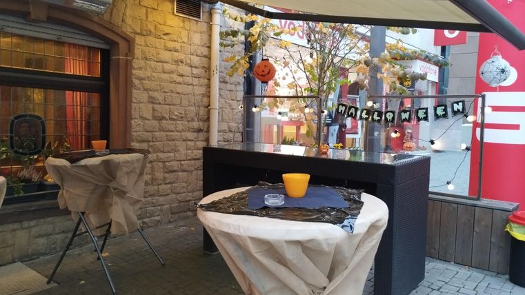 A decorated outdoor area with tables set up for Halloween. The atmosphere is festive with pumpkins and Halloween decoration.